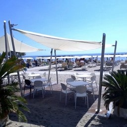 Tavoli e sedie bianche sotto i teli sulla sabbia.