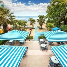 Terrazza con ombrelloni a righe e sentiero verso la spiaggia.