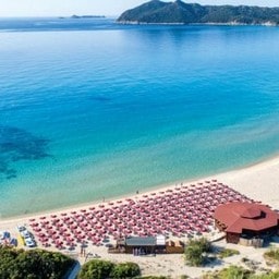 Spiaggia con ombrelloni rossi e mare cristallino vista dall'alto.